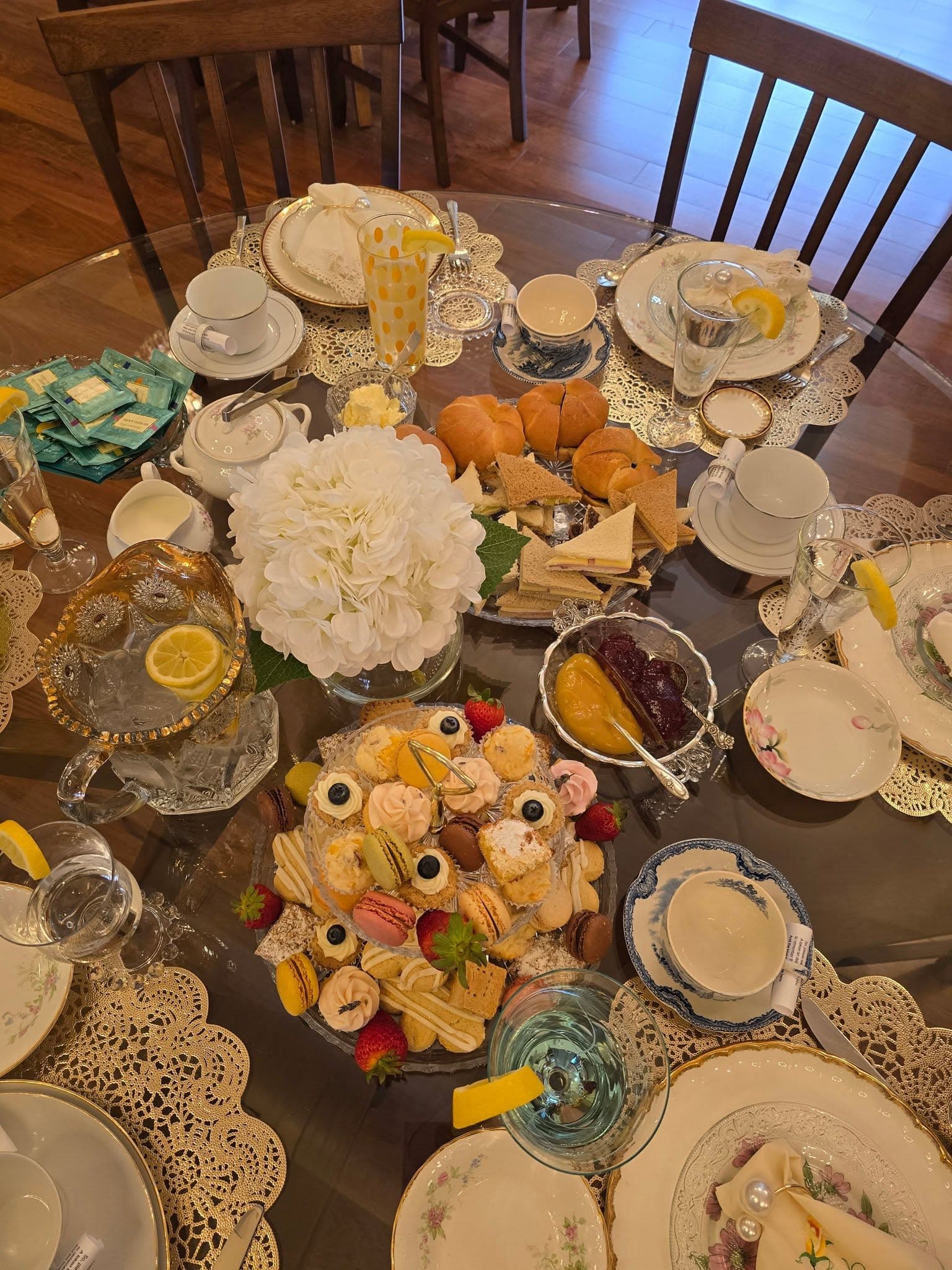 Tea-party arrangement with finger sandwiches, croissants, assorted desserts, teapots, and floral place settings